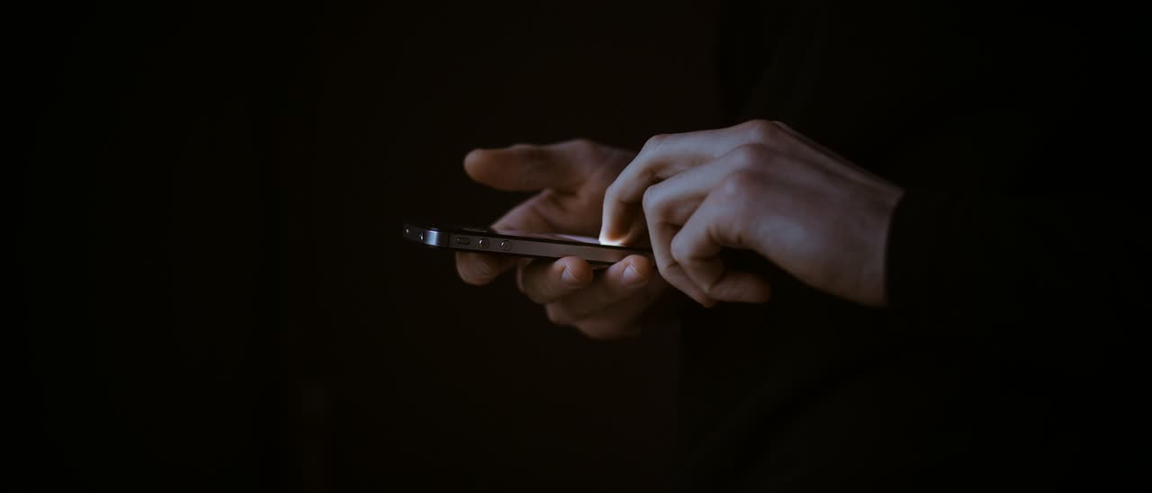 Mãos digitando em um celular no escuro